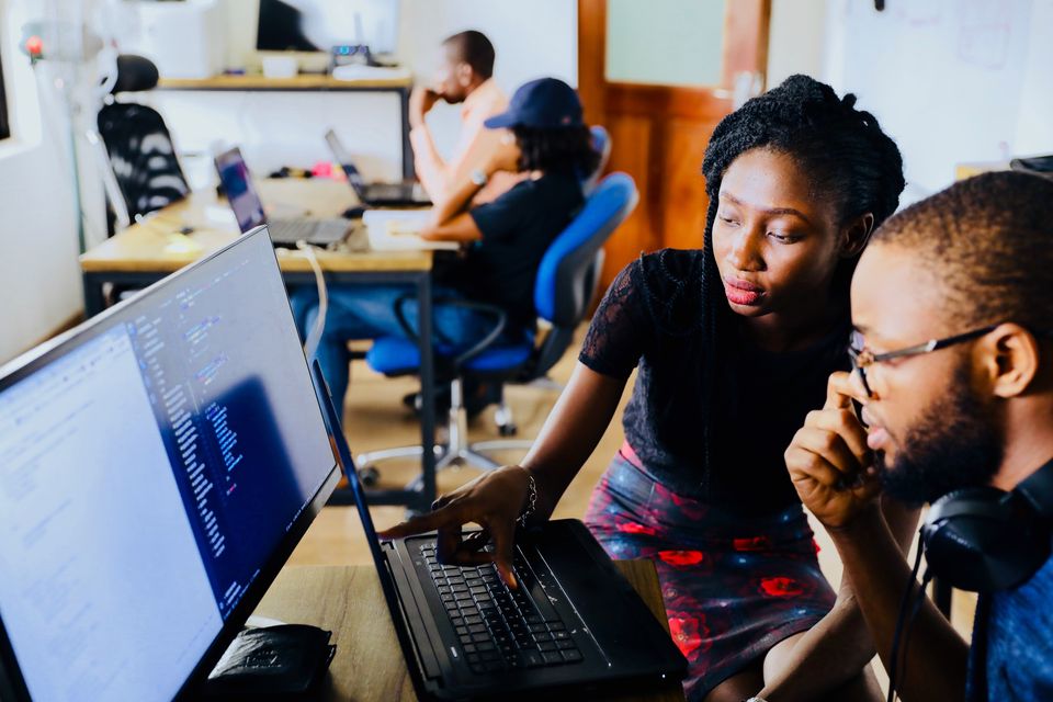 Photo shows two black people collaborating while looking at code in the foreground. Photo by Mars on Unsplash.